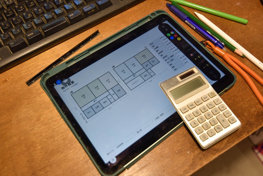 物件の間取り図を映したタブレットと電卓、三角スケール